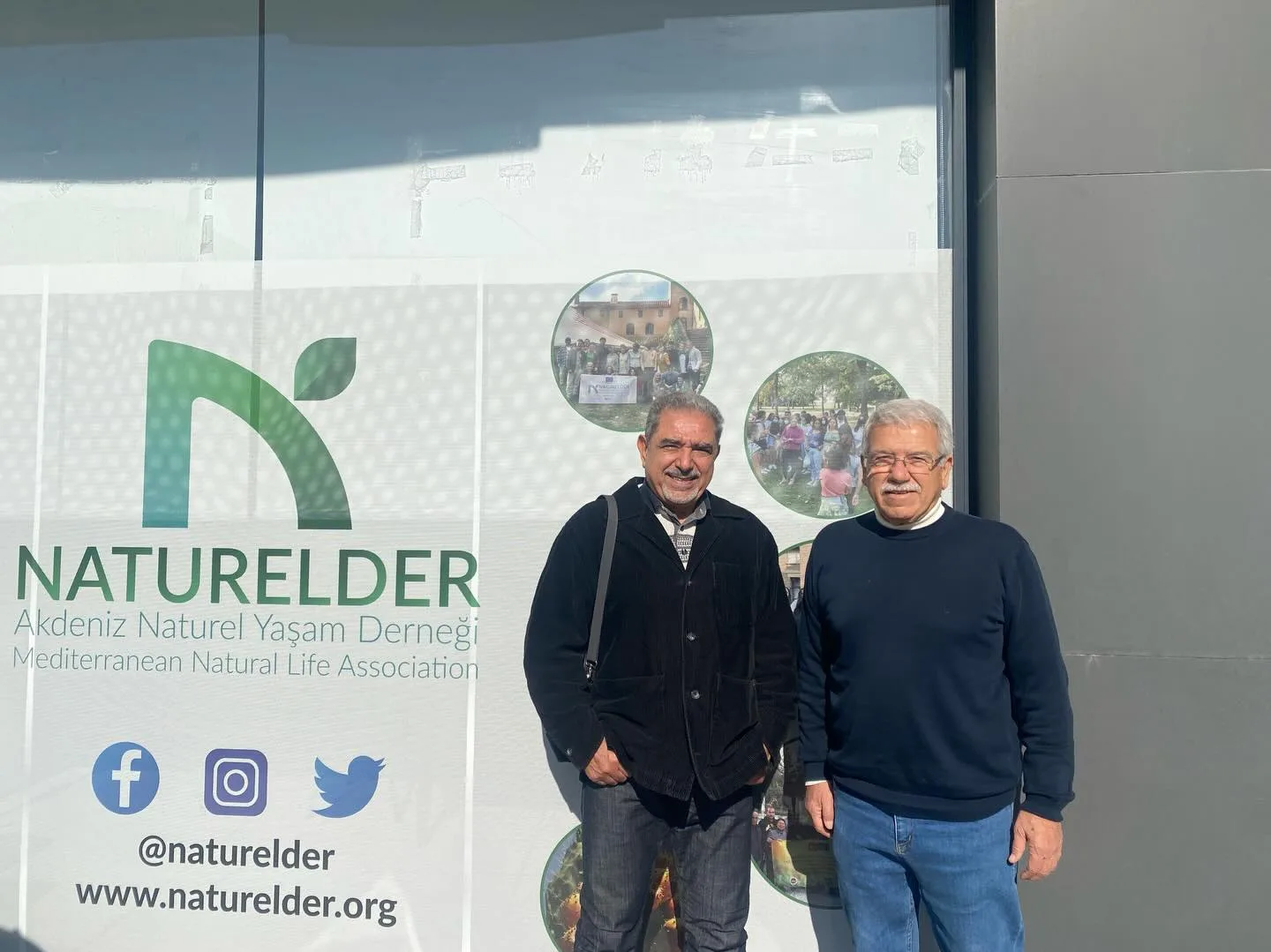 NATURELDER'in girişindeki dernek tabelasının önünde iki ziyaretçi