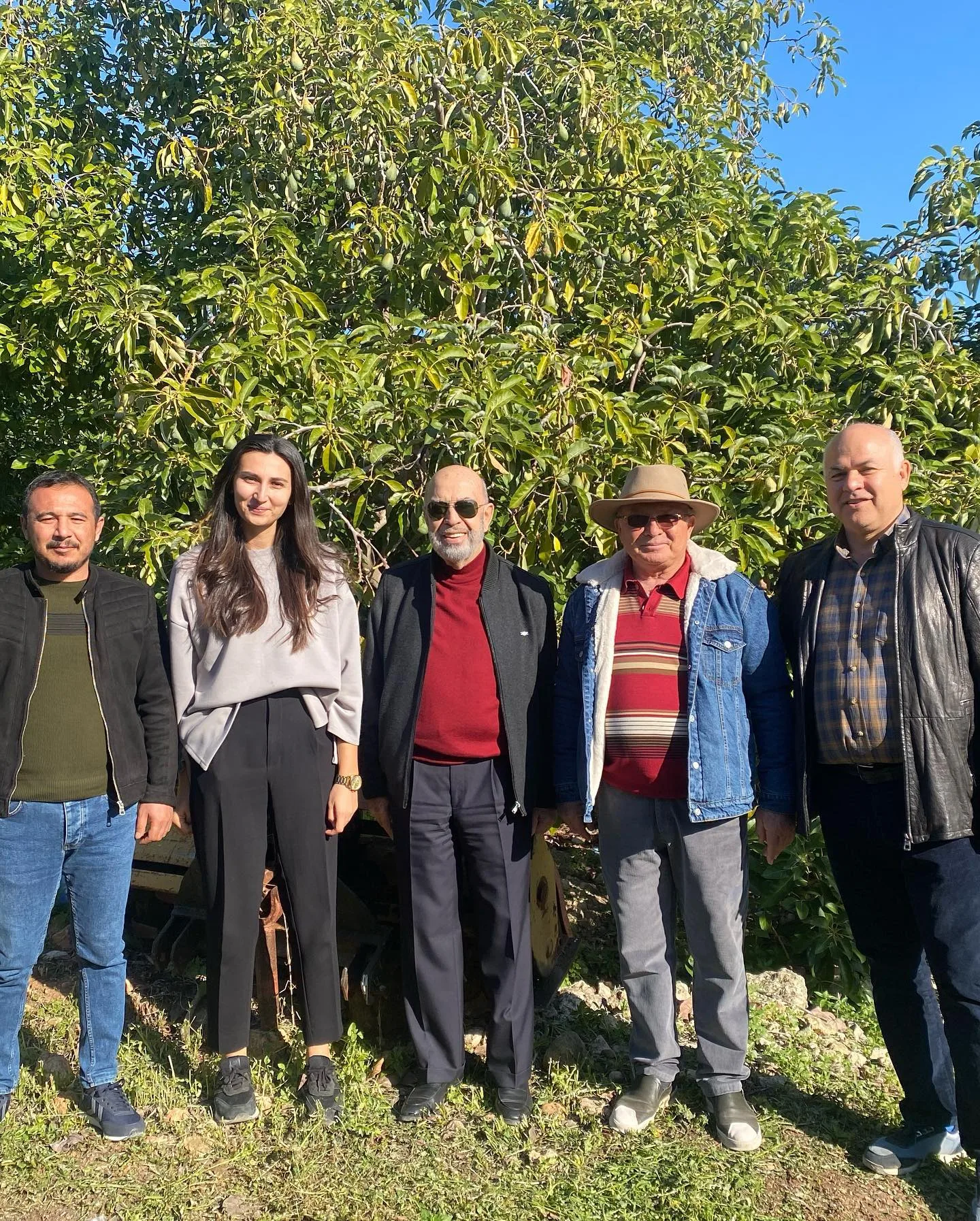 Avokado araştırmasına ilişkin paylaşımda bahçedeki ağaçların önünde bir araya gelen grup