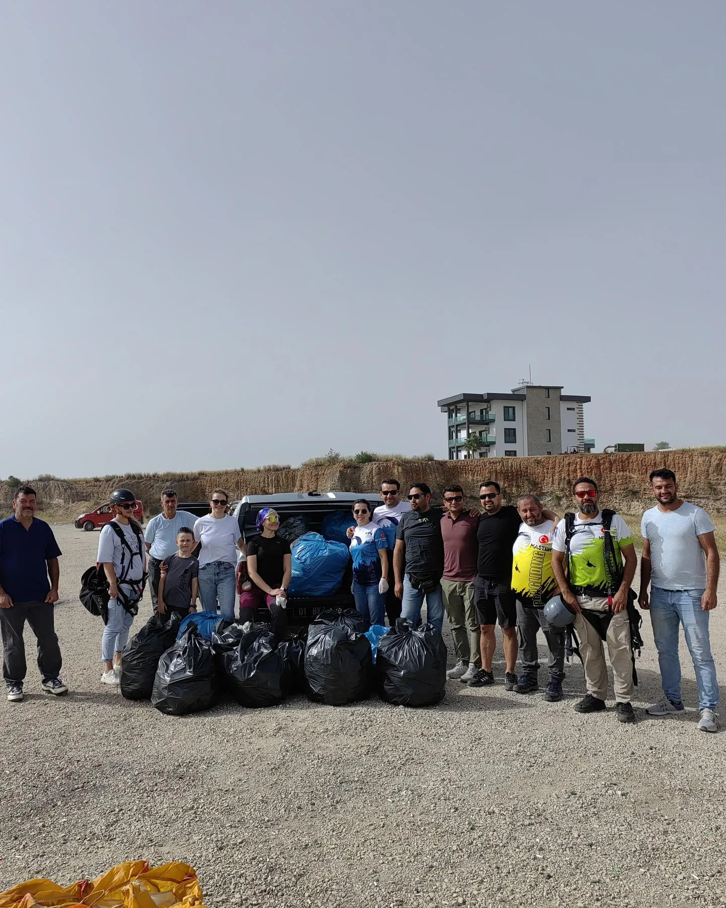 Volunteers gathered outdoors behind filled rubbish bags beside a vehicle