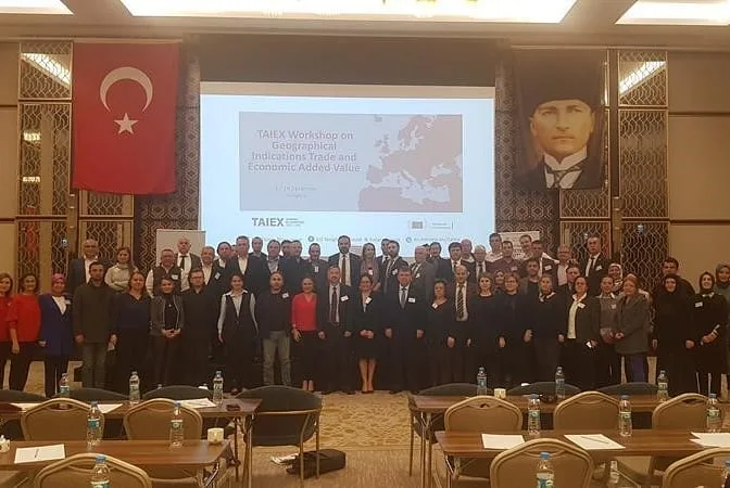 TAIEX coğrafi işaretler çalıştayının başlığını gösteren sunum ekranı önünde toplu fotoğraf için bir araya gelen katılımcılar