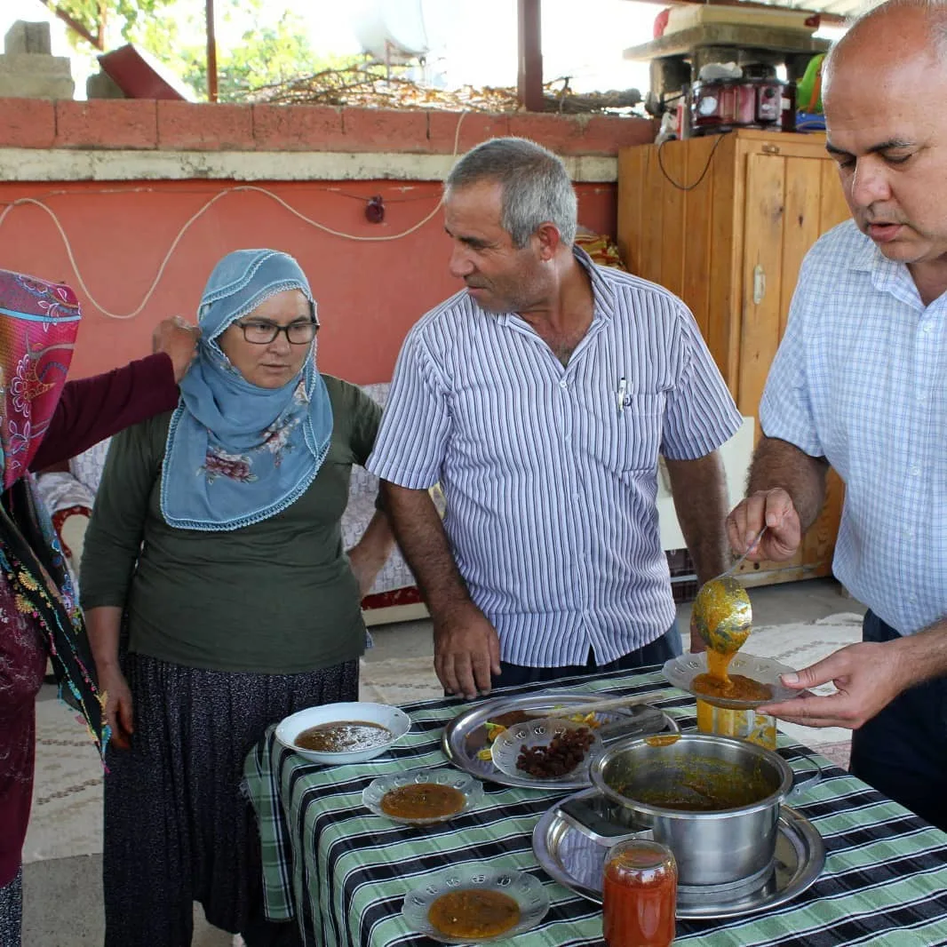 Hazırlanan Hint inciri tatlısının masadaki tabaklara servis edilmesini izleyen katılımcılar